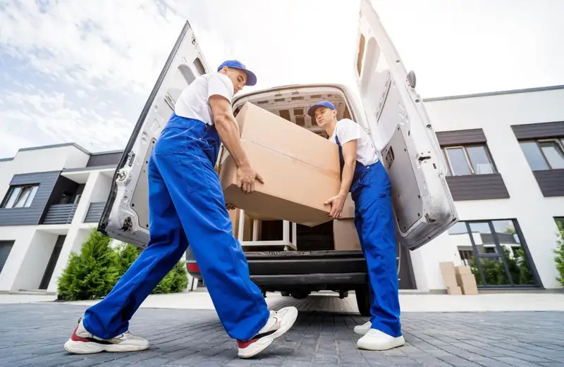 Two movers carrying a large box into a moving van